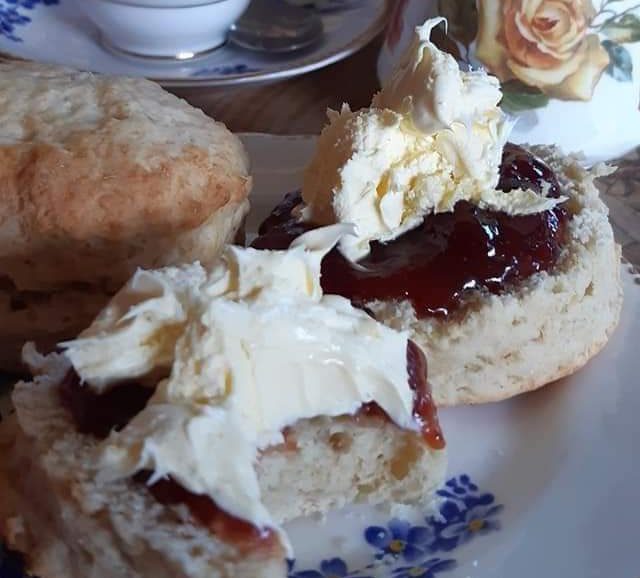 Scones topped with cream and strawberry jam on a floral plate.